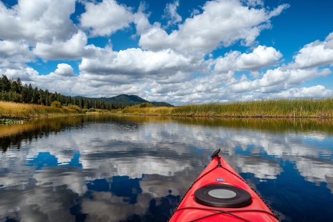 The tip of a red kayak points down a stream at Upper Klamath National Wildlife Refuge under a blue sky.