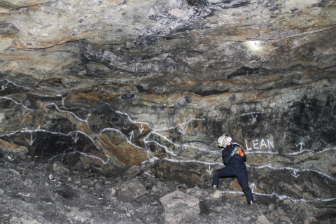 Lone biologist standing along a wall of stone shining a flashlight and looking upward