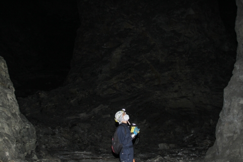 Lone person standing in an underground chamber shining a flashlight and looking up at the ceiling