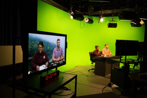 man and woman sitting at news desk with green screen in background of broadcasting studio