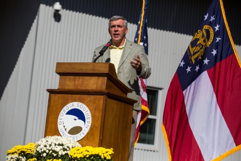 A man in a business suit standing behind a podium speaks into a microphone.