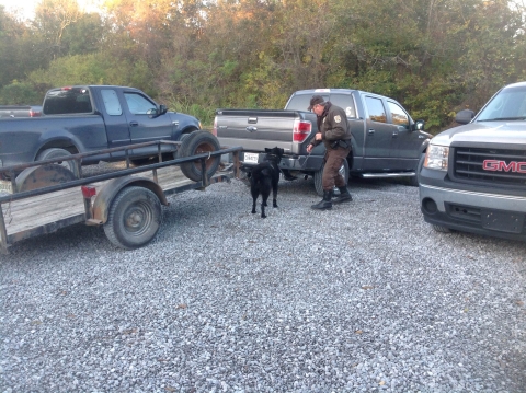  officer and dog look at back of pickup in a gravel lot