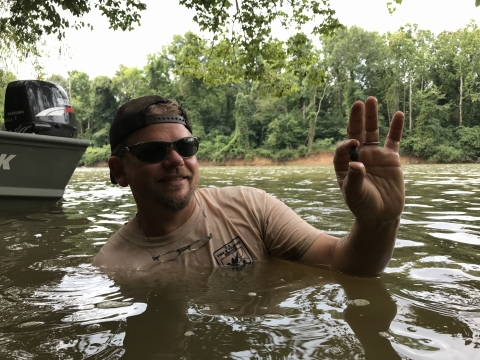 Man swimming in a river holding a small mussel between his finger