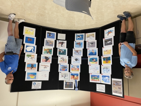 Two volunteers in blue shirts standing next to a junior duck stamp art contest display