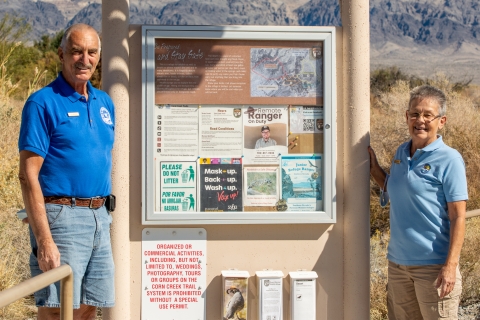 Two volunteers in blue shirts standing next to an information kiosk