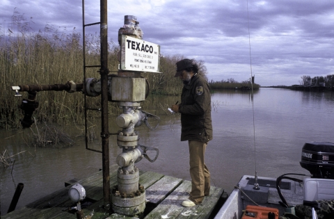 A man stands on an oil drill platform in a channel of water.