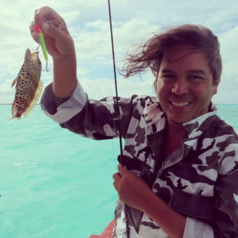 Angelo Villagomez hold s fish attached to a fishing line. The ocean is behind him.