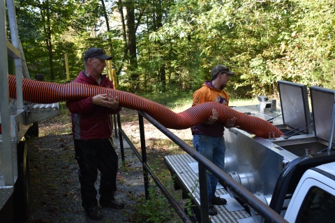 Hatchery personnel transferring trout from truck to truck with stocking hose