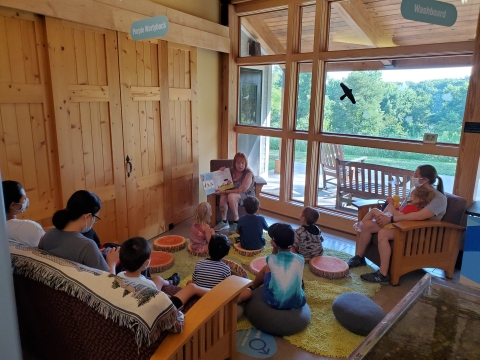 A woman showing a book to a group of kids and parents sitting in front of her