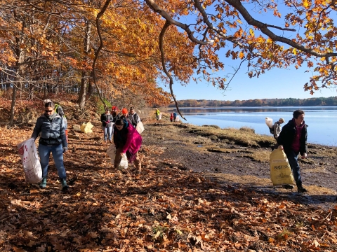 A group of people hold filled trash bags by a shore