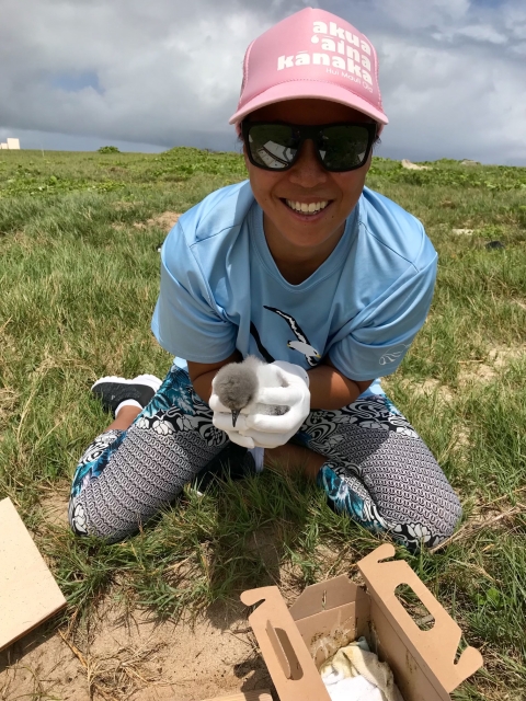 Jiny Kim, wearing a light blue shirt and pink hat, holds a Bonin petrel chick. 