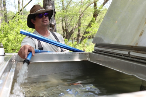 Lone biologist holding a hose with water flowing from hose into a large, metal tank