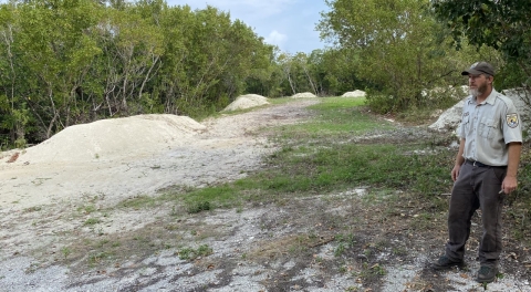 A man in ballcap and uniform looks over a field with raised, sandy mounds.