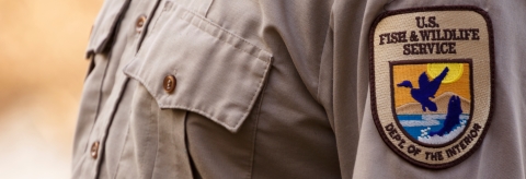 A close up of a U.S. Fish and Wildlife Service staff wearing the Service uniform's beige shirt with the shield patch on the shoulder. 