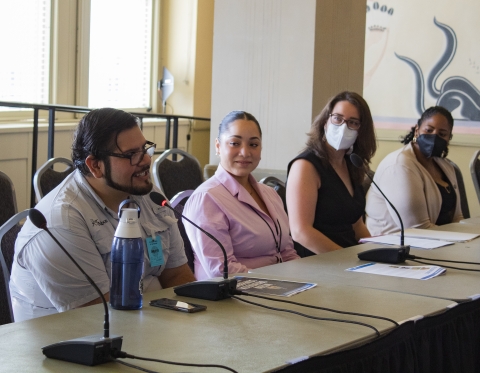 Four people in formal attire with microphones speaking at a panel discussion