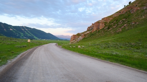 Winding dirt road across a field with mountains in the distance.