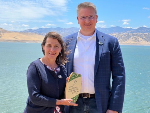 two people stand outside for a photo with a wooden award