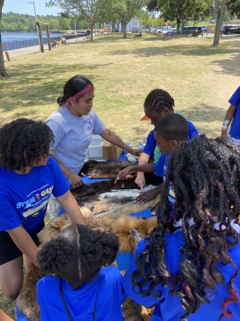 A young woman teaching a group of students about wildlife fur at an outdoor table