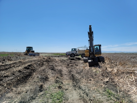 A truck and two pieces of heavy machinery on a flat refuge field on a clear day.