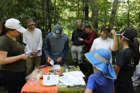 a group surrounds a folding table, littered with supplies for banding birds 