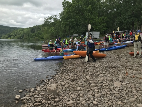 A group of people prepare to launch kayaks on a cobble river beach