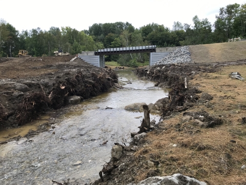 a river flows with steep banks on either side flowing under a bridge.