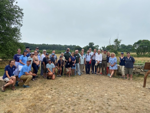 A group of about 30 people gathers in front of an open field. Some kneel, others stand. Everyone is smiling. 