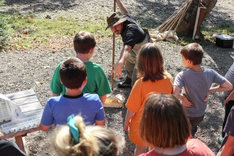 Lone adult standing before a group of students holding a small net with a long handle