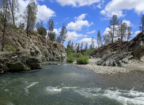 landscape photo of a river surrounded by rocks and a cloudy blue sky