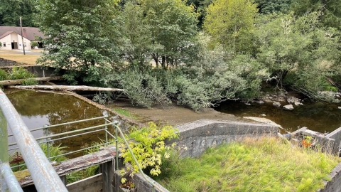 A dam with trees along the bank and a house in the background