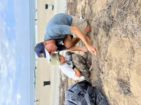 a boy and a man crouched down on dune removing weeds