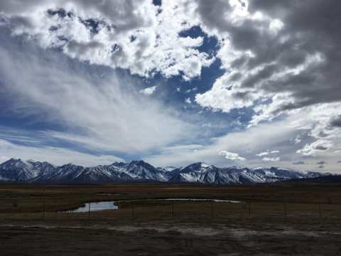 A small river in a dry landscape with a large, snowy mountain range in the distance.