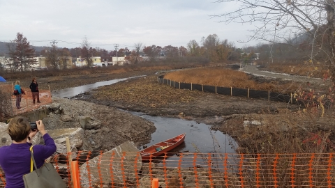 a river weaves through a landscape covered in dirt, dead vegetation, and plastic construction fences