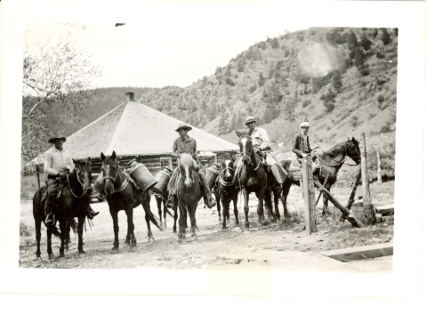 Men on horseback with milk cans of fish hanging on the sides for transport