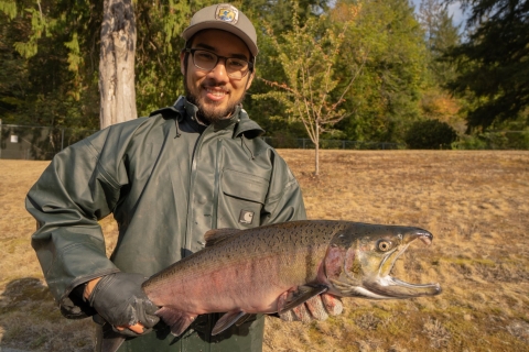 Intern Eric Klingberg poses holding a adult coho salmon at the Quilcene National Fish Hatchery in Quilcene Washington.