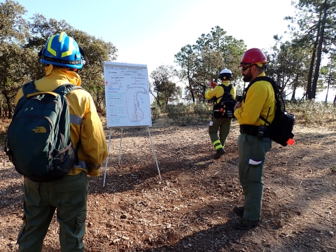 2 firefighters at whiteboard; 3rd walks away