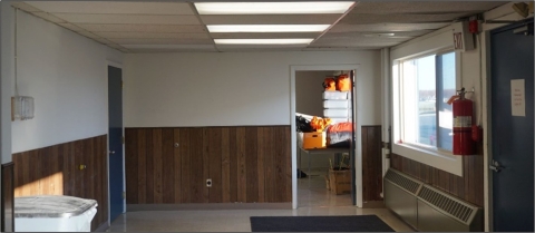 View of office space inside a hangar. Window to the left and open storage room door to the rear. 