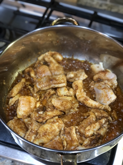 A skillet filled with cooked fish in a brown sauce.