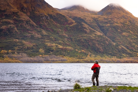 A woman fishing in a lake with mountains in the background