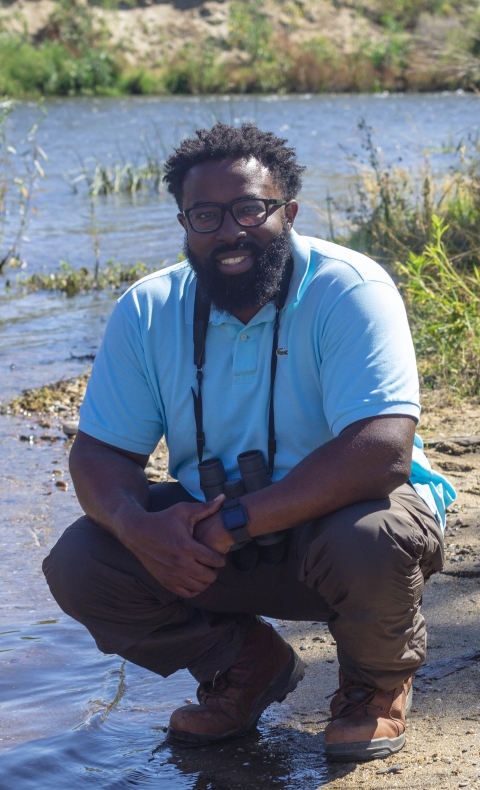 A man in a blue shirt crouching down with a pair of binoculars