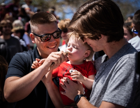 Two adults smiling while holding a razorback sucker for a baby to kiss