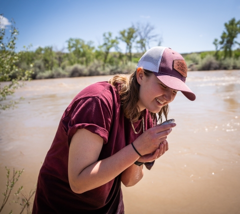 A person smiling while holding a razorback sucker. River in background.