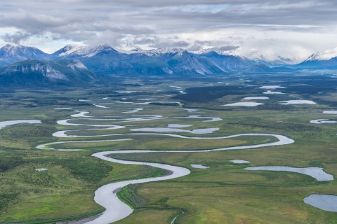 A river twists and turns across a plain bordered by snow-capped mountains.