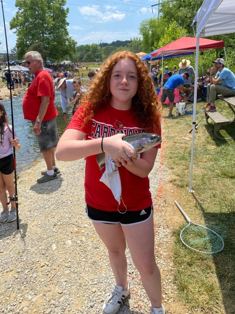 Girl holds rainbow trout beside stream