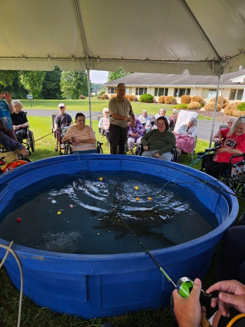 Elderly people fishing out of blue stock tub under a tent