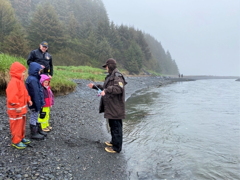 woman in USFWS uniform shows kids a fishing pole by a river