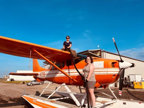 one person sitting on top of and a second person standing in front of an airplane