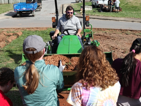 Man on a tractor with people placing rolled sod in the front-end loader