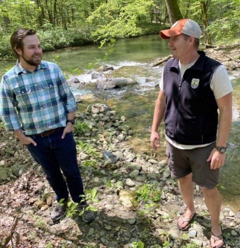 Two men alongside a creek in the forest.