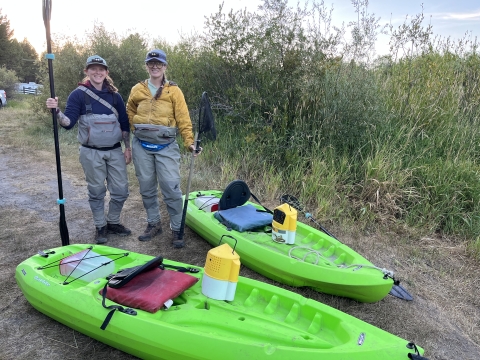 Two women with paddles in front of two kayaks